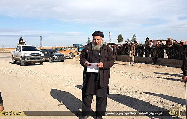 A supposed ISIS cleric reads out charges against a man accused of witchcraft shortly before his execution in a rural area named Aldbsa, to the west the city of Raqqa. (Photo Credit: Mail Online)