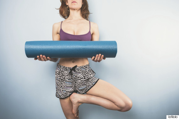 Woman in tree pose holding a yoga mat