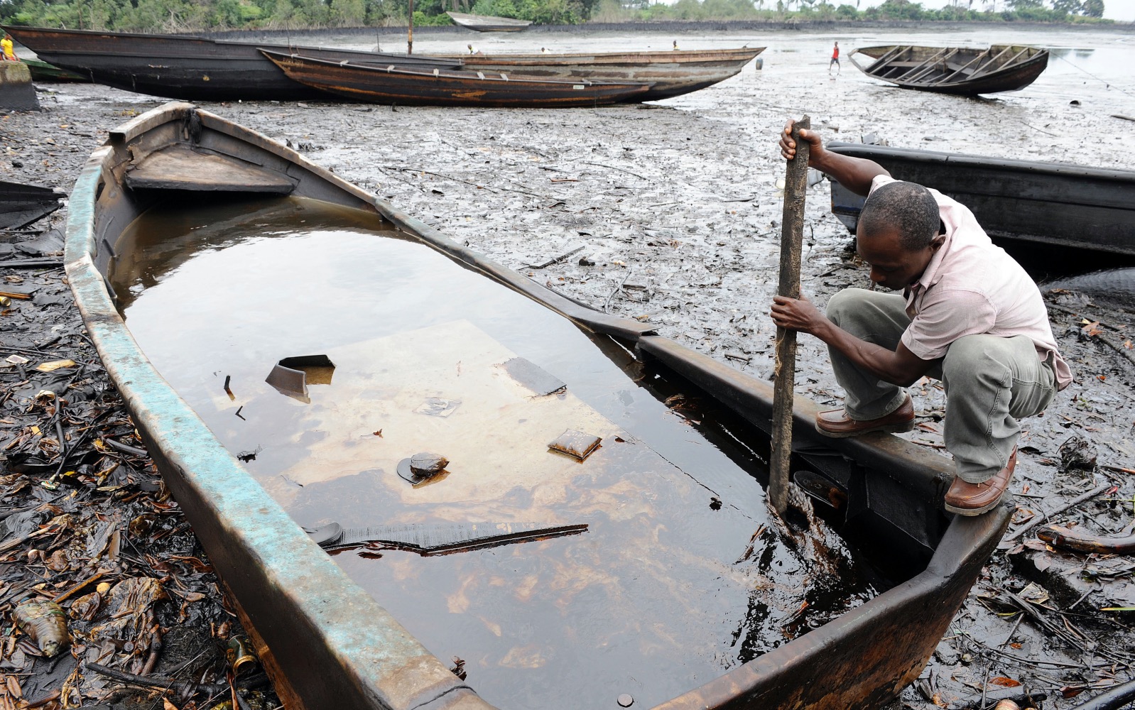 Niger Delta: An indigene of Bodo, Ogoniland region in Rivers State, tries to separate with a stick the crude oil from water in a boat at the Bodo waterways polluted by oil spills attributed to Shell equipment failure August 11, 2011 | AFP/Pius Ekpei