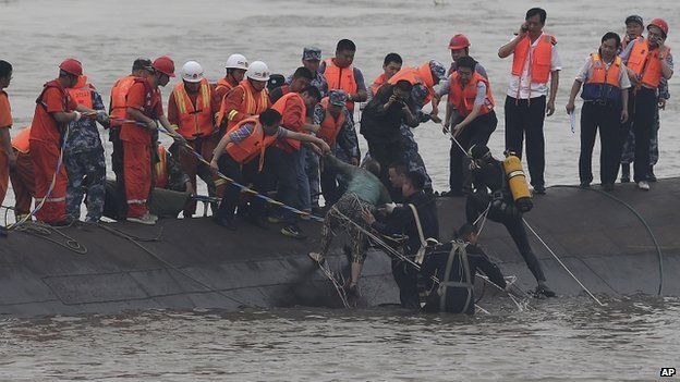 Rescuers standing on the capsized ship's hull pulling out a 65 year old woman (Credit: BBC/AFP)