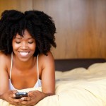 A black woman lying in bed using a cell phone.