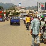 Burundi, Bujumbura, vehicles with people on road with houses in background in city. (MR)
