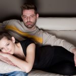 couple watching tv couch unhappy