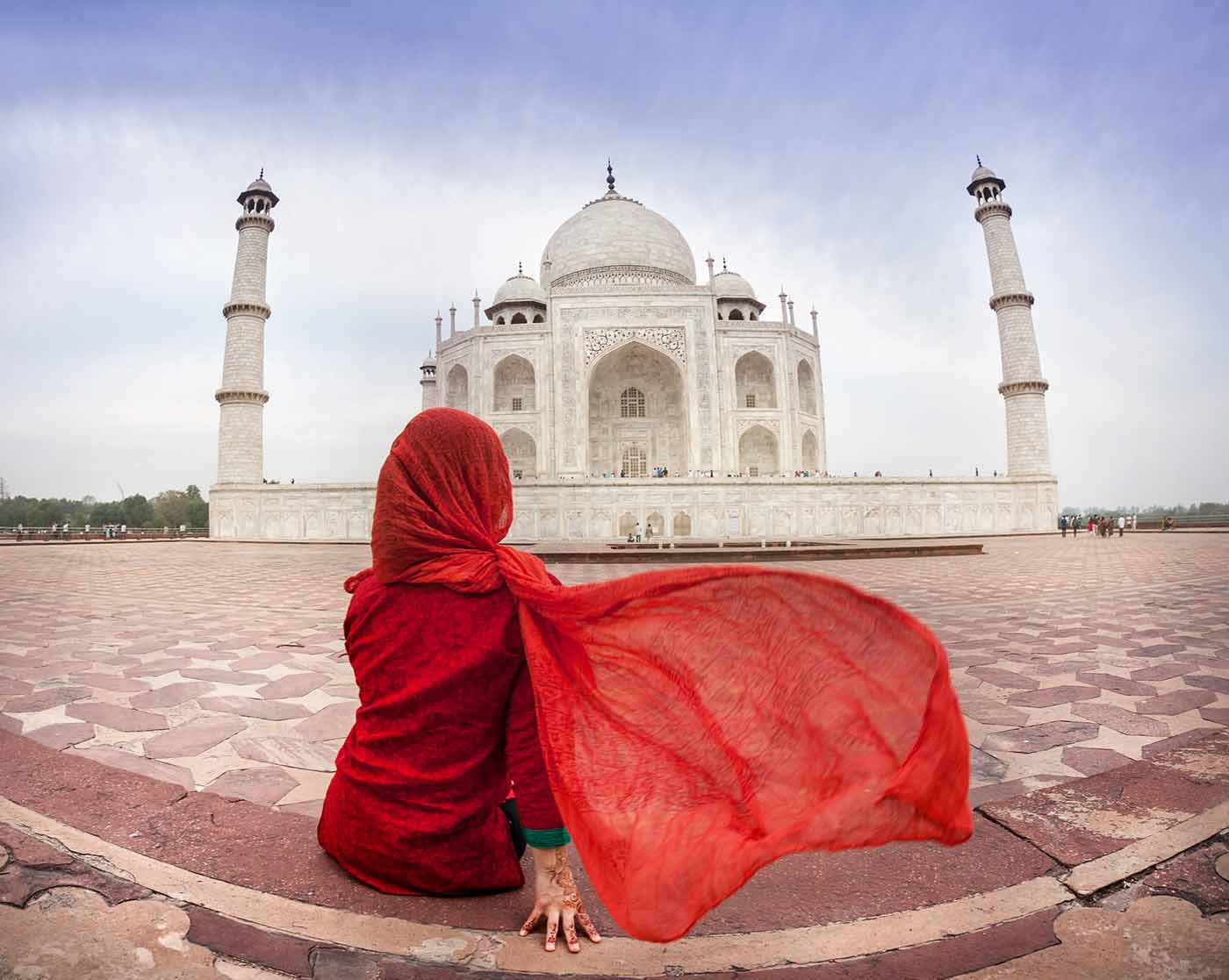 Woman in red costume with flattering scarf sitting near Taj Mahal in Agra, Uttar Pradesh, India