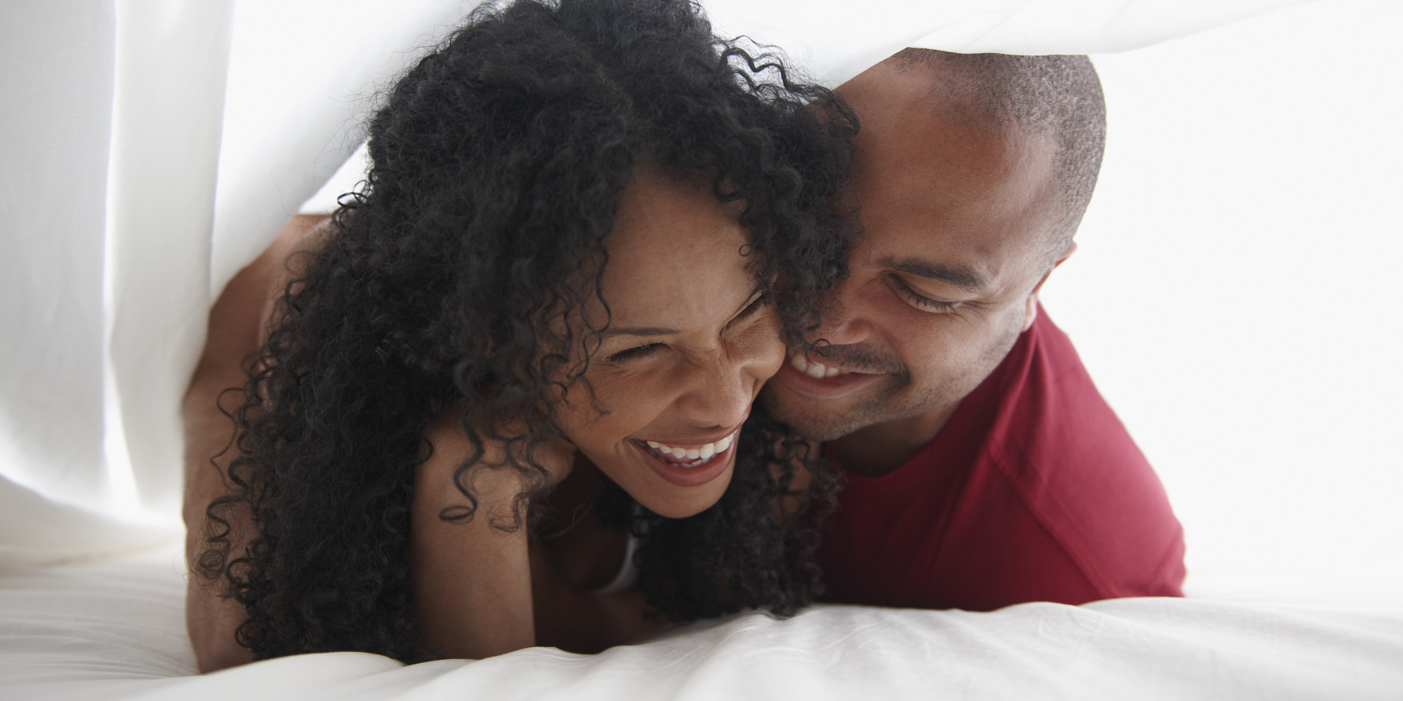 Smiling Black couple underneath sheet