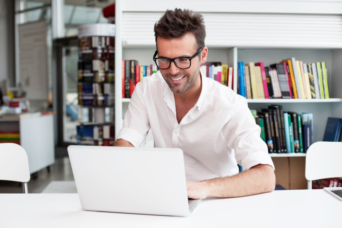 Happy man working on laptop in library