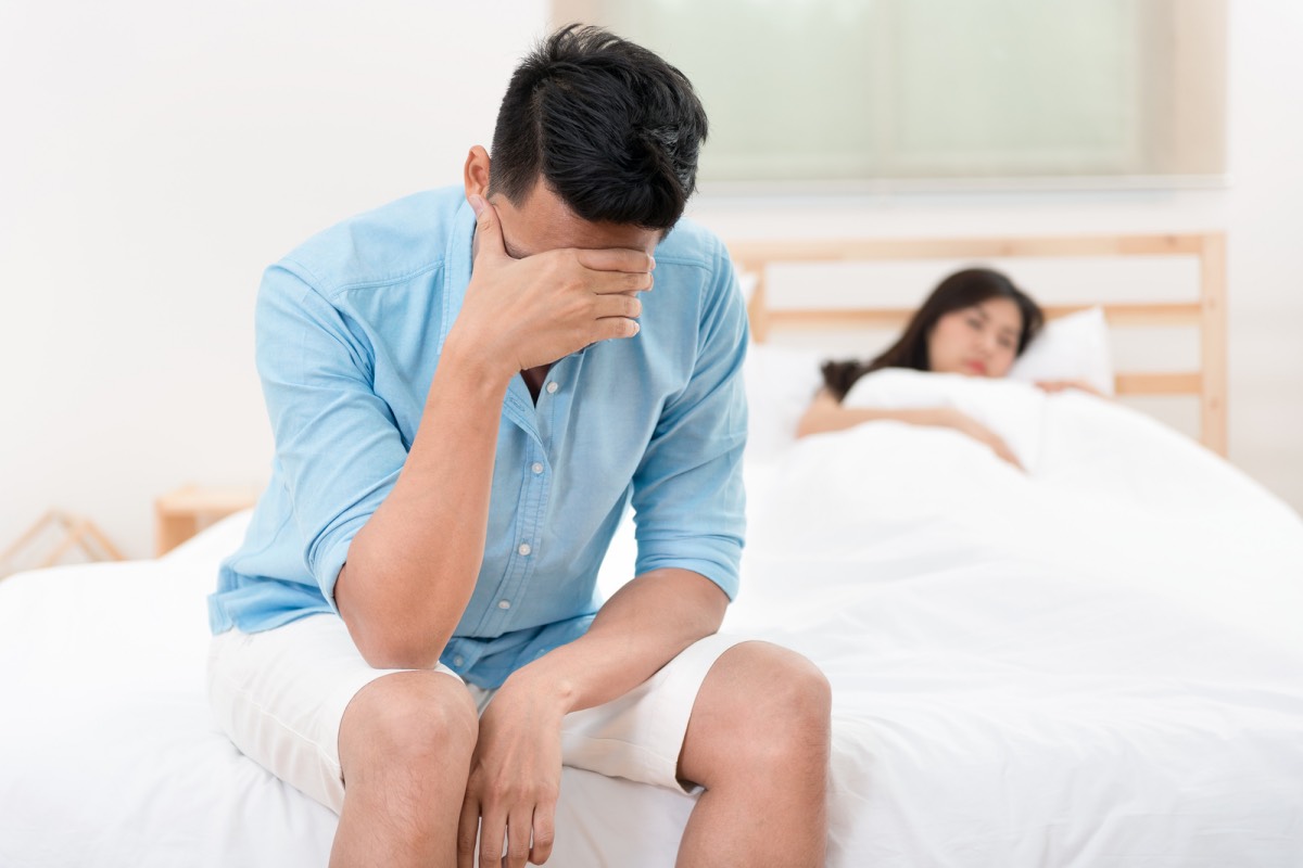 Husband unhappy and disappointed in the erectile dysfunction during sex while his wife sleeping on the bed. Sexual Problems in Men.