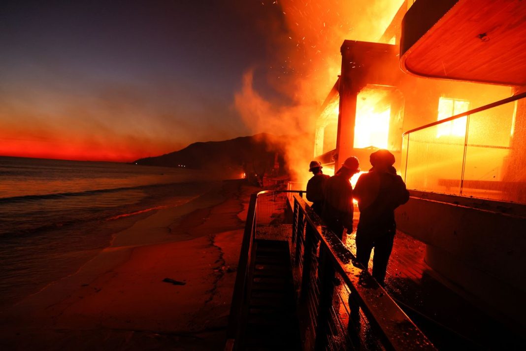 Firefighters work from a deck as the Palisades Fire burns a beach front property in Malibu, California on Wednesday, January 8, 2025. | Etienne Laurent/AP