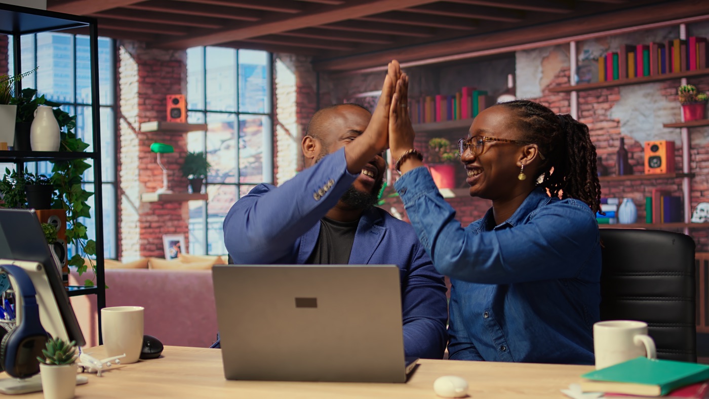 Black freelancing couple doing a high five to celebrate intimacy their achievement, completing tasks to ensure successful project. Young man and woman feeling pleased with their cooperation. Camera A.