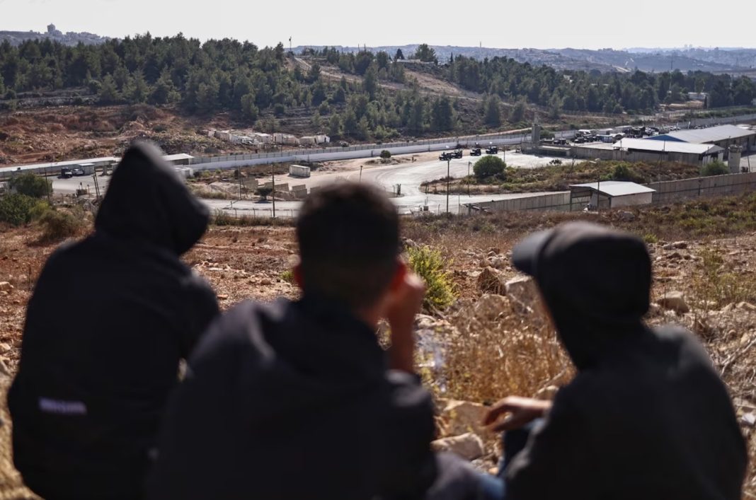 Palestinian youths watch as an Israeli forces take position at the Ofer military prison, located between Ramallah and Beitunia in the occupied West Bank, ahead of the release of Palestinian prisoners on Monday, October 13, 2025. | Zain Jaafar/AFP/Getty Images