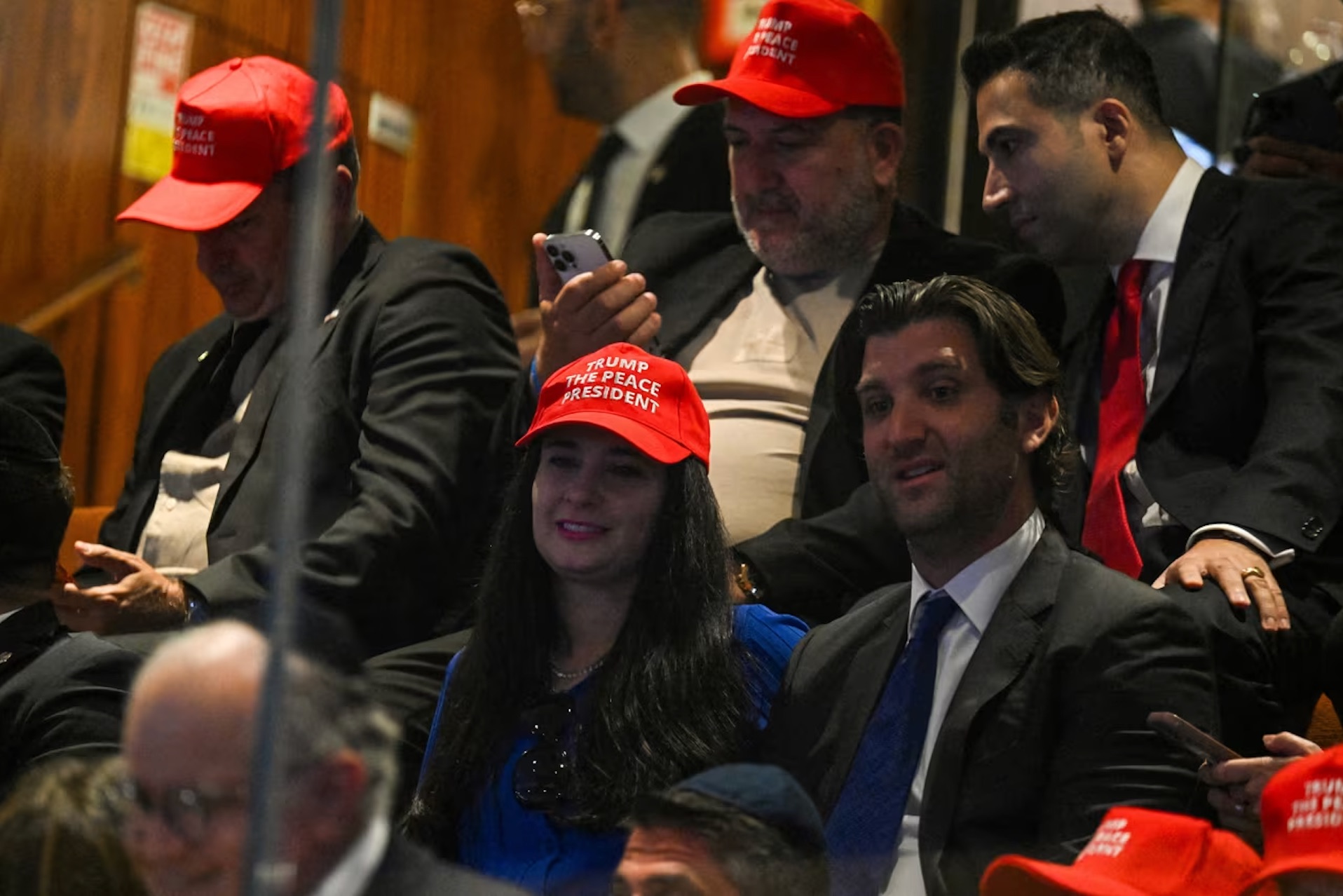 People wearing hats reading "Trump The Peace President" sit inside the Knesset, on Monday, October 13, 2025. | Kenny Holston/Reuters