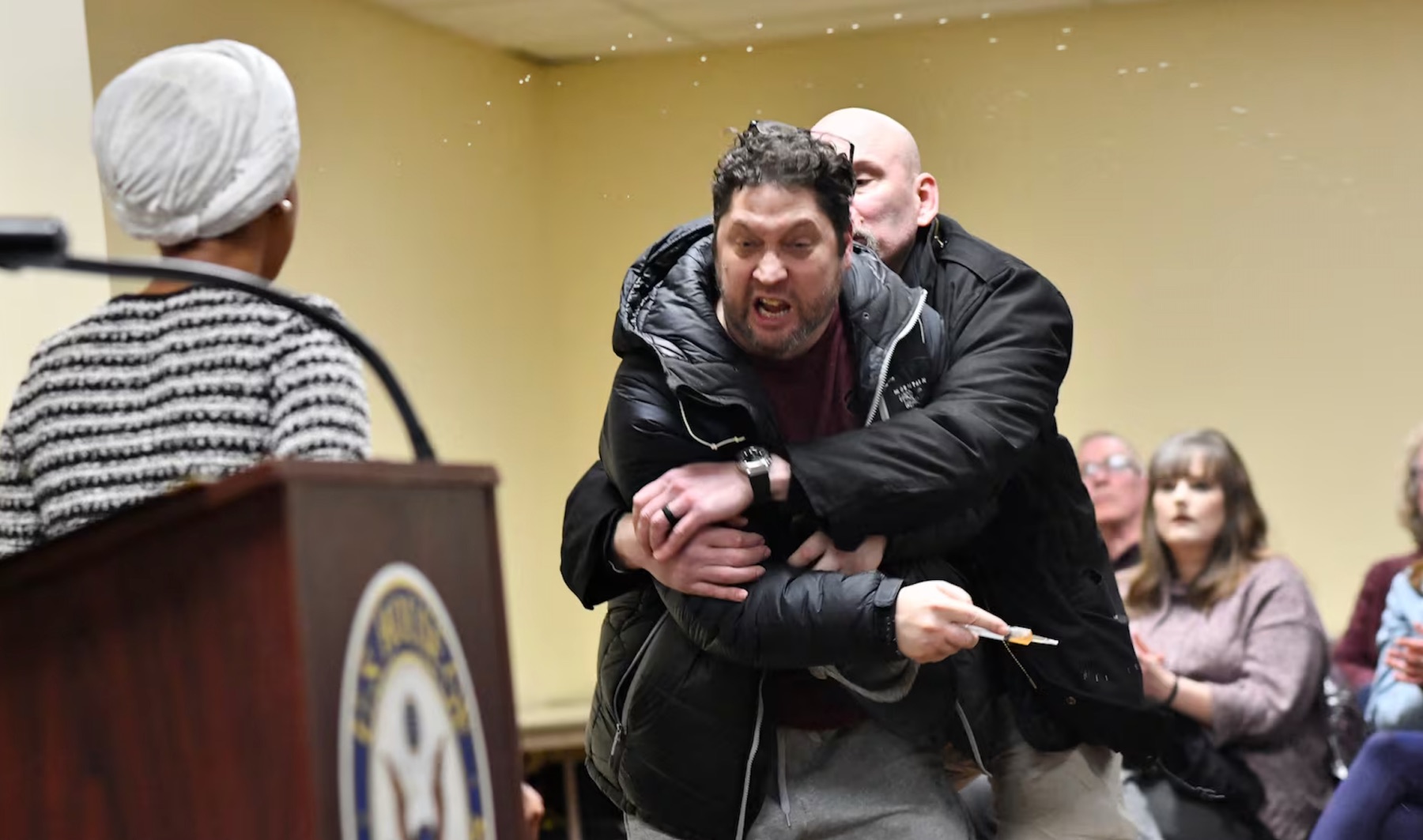 55-year-old Anthony Kazmierczak is restrained by security after allegedly attempting to spray Representative Ilhan Omar with a liquid during a town hall meeting in Minneapolis on January 27, 2026. | Octavio Jones/AFP via Getty Images