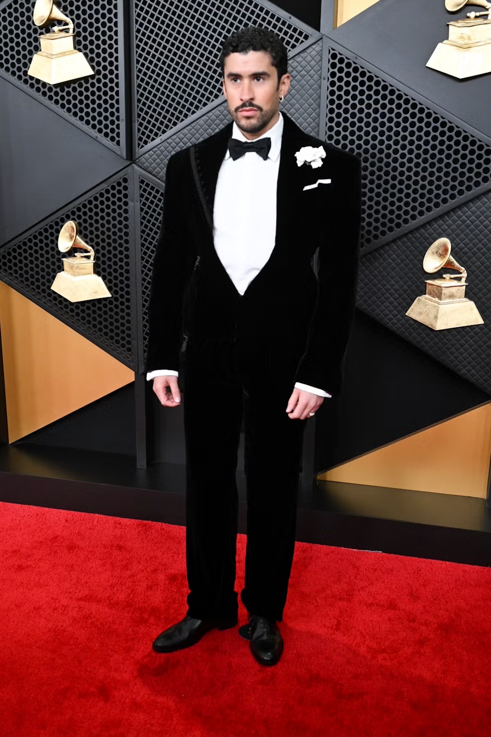 LOS ANGELES, CA – FEBRUARY 2026: Bad Bunny arrives on the red carpet at the 2026 Grammy Awards, wearing a classic black tuxedo with a white floral accent. | Gilbert Flores/Getty Images