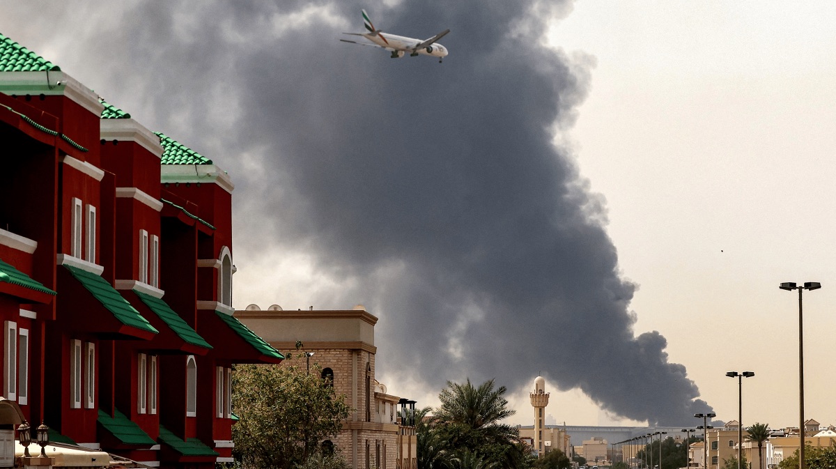 An Emirates aircraft flies above smoke rising from the Fujairah oil industry zone after debris from an intercepted drone caused a fire, in Fujairah, United Arab Emirates, on March 4, 2026. | Amr Alfiky/Reuters