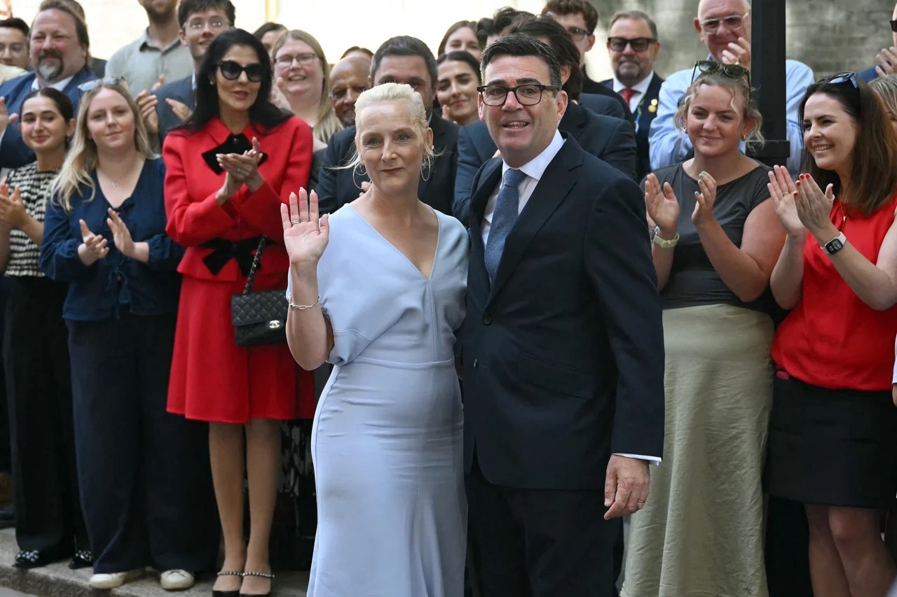 New British Prime Minister Andy Burnham and his wife, Marie-France van Heel, are welcomed by staff as they arrive inside 10 Downing Street in London on