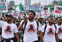 Former Minister Blasts Borno Governor Over Arrests of ‘Tinubu Must Go’ T-Shirt Wearers An illustration generated with artificial intelligence shows Nigerian youths wearing “Tinubu Must Go” shirts and carrying placards during a street protest. | The Trent